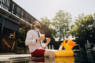 Businessman relaxing in swimming pool with inflatable duck and cocktail