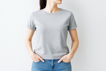 Obraz premium Woman in plain gray t-shirt with rolled sleeves and jeans standing against white wall background for branding or t-shirt design mockup concept.