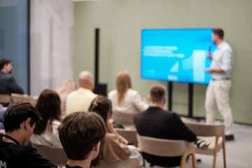 Fototapeta premium Audience listening to speaker presenting in a contemporary seminar setting, fostering engagement.