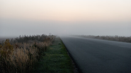 Empty road in morning fog. Diminishing perspective view of a rural road in foggy meadow in the morning.