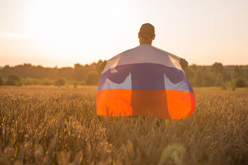 Patriotism. A man with a Russian flag in a wheat field at sunset. The concept of planting and...
