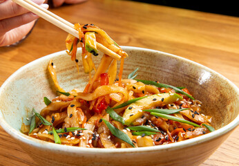 Eating noodles with vegetables with chopsticks.