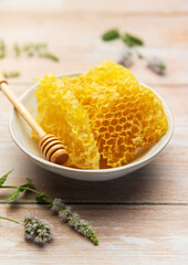 Honeycomb in bowl with honey dipper and fresh mint on wooden table