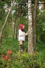 Young girl with pink hair exploring forest and touching tree trunk