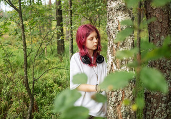 Young relaxed girl listening music leaning against birch in forest