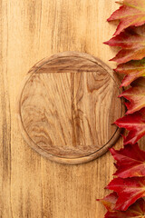 A rustic wooden crooked pizza board placed on a vintage wooden background, decorated with vibrant autumn leaves symbolizing the harvest season and Thanksgiving.