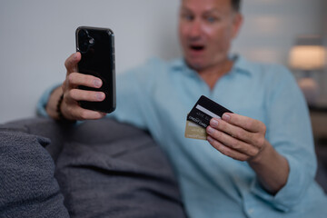 Shocked mature man is checking his online banking account on his smartphone after shopping online...