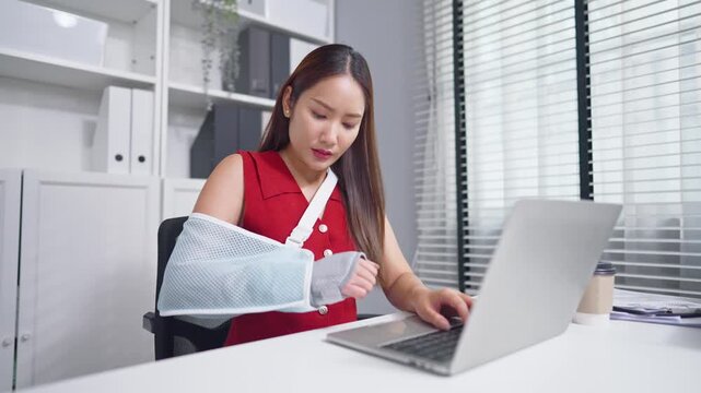 Asian businesswoman wearing hand splint and using laptop in the office