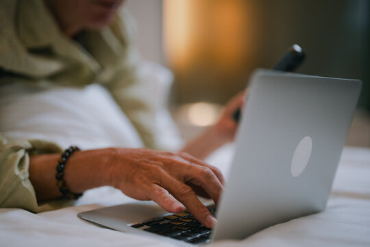 Businessman lying in bed and working from home, using a laptop and smartphone. Typing on the keyboard while holding the mobile phone, balancing productivity and comfort