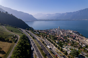 Lake Geneva in Switzerland seen from above with French Alps in the background on a sunny hazy day and Montreux cityscape below the freeway in the foreground
