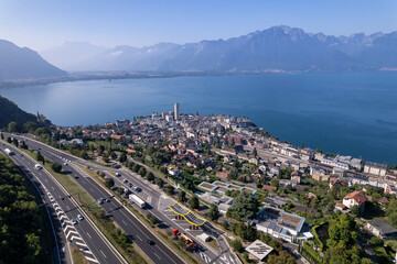 High mountains of French Alps in the background of Montreux cityscape at Lake Geneva in Switzerland seen from above on a sunny hazy day and below the a9 freeway in the foreground