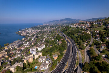 Montreux cityscape at Lake Geneva in Switzerland seen from above with French Alps in the background on a sunny hazy day and below the a9 freeway in the foreground