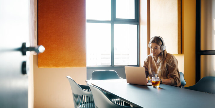 Young woman working on a laptop with headphones in a modern office