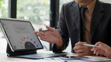 Two business professionals collaborating on a digital tablet in a modern office setting, emphasizing teamwork and technology. - Powered by Adobe