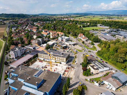 Aerial view of urban sprawl meets verdant countryside, where terracotta roofs contrast with modern architecture and a construction site buzzes with activity, Aarberg, Canton of Bern, Switzerland.