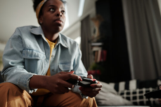 Low angle view shot of young African American woman spending free time at home playing video games