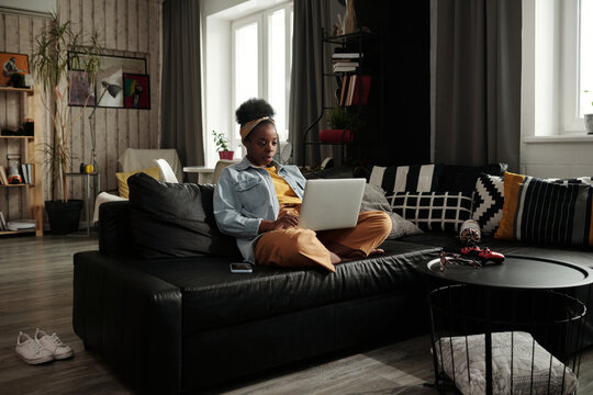 Horizontal long shot of young African American woman spending time at home during lockdown surfing Internet on laptop, copy space