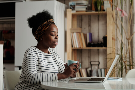 Portrait of young African American woman spending time at home sitting at table in front of laptop having video call