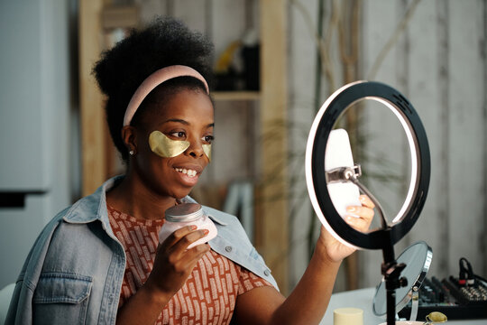 Medium close-up portrait of modern African American woman with golden patches under eyes taking selfie pictures on smartphone
