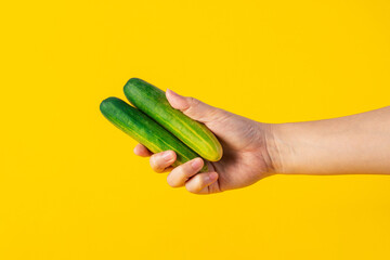 Fresh green cucumber in hand on yellow background