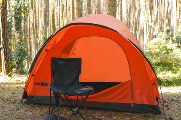 Bright orange tent nestled and set up in a lush green forest, camping in the woods.