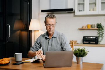 Lifestyle people, Mature male working sitting in the kitchen. with laptop and documents on desk, small business owner working online.