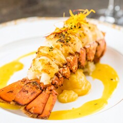 Tender baked lobster with a cheesy topping, served on a beautiful plate with a rich, creamy yellow sauce.
