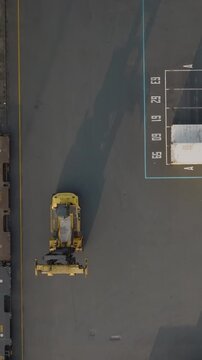 Aerial view of a straddle carrier moving shipping containers in a port terminal. The machinery is transporting cargo for import and export logistics. Country: Unknown.
