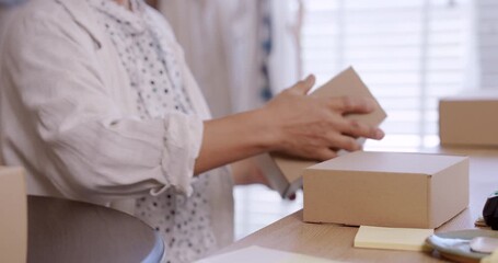 Closeup hands of senior asian woman sealing cardboard box inside boutique studio ecommerce shipping preparation small business teamwork branding handmade fashion entrepreneurship family inventory