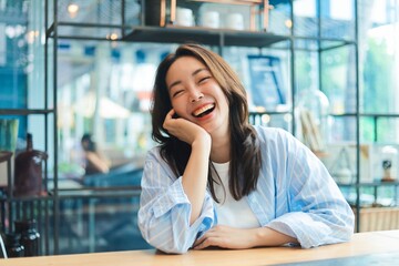 . Portrait Cheerful Asian woman smiling at modern cafe, representing freelance lifestyle, digital nomad, and online business success.