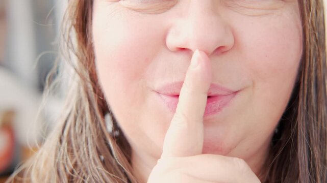 Woman 50 makes shh gesture with finger to lips, signaling silence and discretion, parts of female face close-up, elderly woman with wrinkles, powerful non-verbal cue, keep quiet, secret keeper