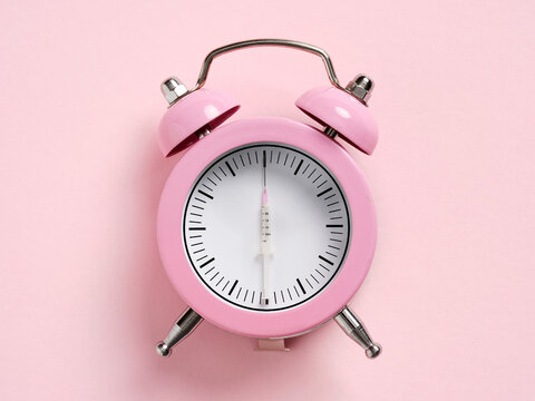 Pink alarm clock with syringe as hour hand showing the importance of scheduled medication