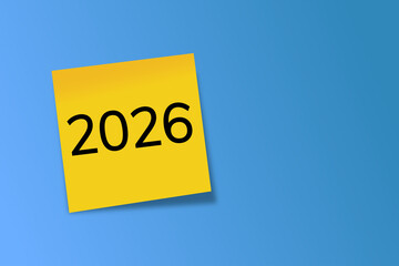 2026. goals. plan. new year. A yellow sticky note with the number “2026” written in bold black font, placed on a squared notebook paper background.