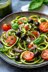 Zucchini Noodle Salad with Cherry Tomatoes and Basil Pesto, fresh zucchini noodles tossed with cherry tomatoes, black olives, and sliced red onions, coated in a homemade basil pesto.