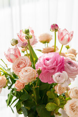 Close-up delicate bouquet of pink and peach flowers gently lit by sunlight, featuring blooming ranunculus