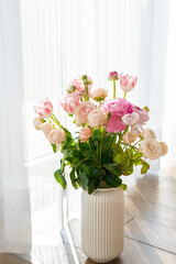 Elegant bouquet of ranunculus blooms in soft pastel hues standing win a white vase, reflecting romance and tenderness