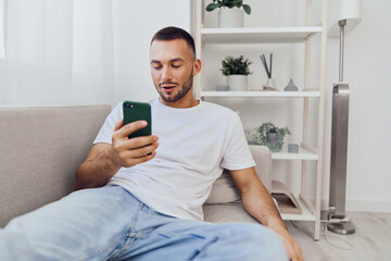 Casual man using smartphone in a modern living room, engaged and relaxed, surrounded by greenery and soft light, perfect for lifestyle themes and trends.
