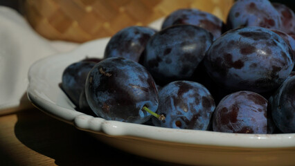 Close-up of fresh plums in a white ceramic bowl on a wooden surface. Summer harvest illuminated by soft natural light