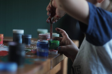 Small child drawing with paints on white paper.
