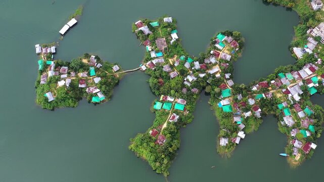 Aerial view of houses with colorful roofs scattered across lush green islands surrounded by calm water, Rangamati, Chittagong Division, Bangladesh.