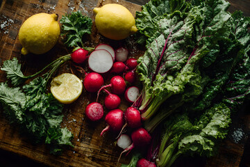 Fresh vegetables with leafy greens and radishes scattered on rustic board perfect for cooking blog and healthy content