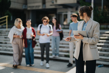 A professor holding a tablet engages with a group of university students outdoors, illustrating academic discussions. The casual setting conveys collaboration, education, and interaction.