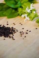 Basil seeds on wooden table with fresh leaves and blooming flowers.