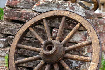 Close-up of an old wooden wagon wheel leaning against a stone wall, rustic vintage detail.
