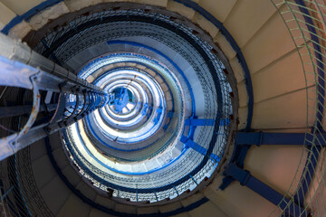Fototapeta premium Abstract industrial spiral interior view, upward view of large circular metal structure with repeating geometric patterns and blue tones.