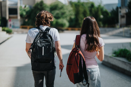 Two young people walking outdoors on a bright day, carrying backpacks, and engaging in conversation. Depicts a campus environment and portrays an academic setting, collaboration, and student life.