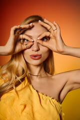 Fototapeta premium Stylish woman playfully posing with hands framing her face against a colorful backdrop