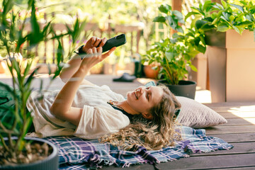 Beautiful young woman with a mobile phone in her hands lying on the summer terrace of a country house © olezzo