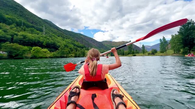 Girl paddling a kayak on a calm lake surrounded by mountains, enjoying a sunny day of outdoor activity