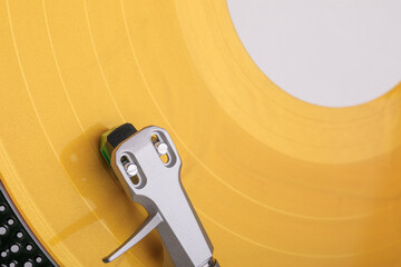 Macro photo of bright yellow vinyl record spinning on turntable with silver tonearm and green stylus, showcasing grooves and texture.
